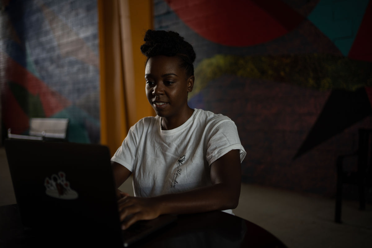 woman types on a black laptop in white shirt