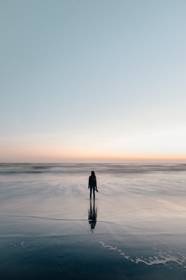 woman wades in ocean at sunset