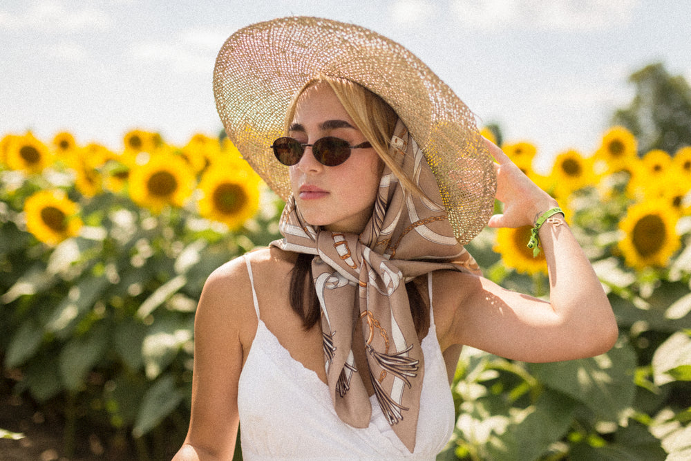 woman wearing a silk scarf stands in a field of sunflowers