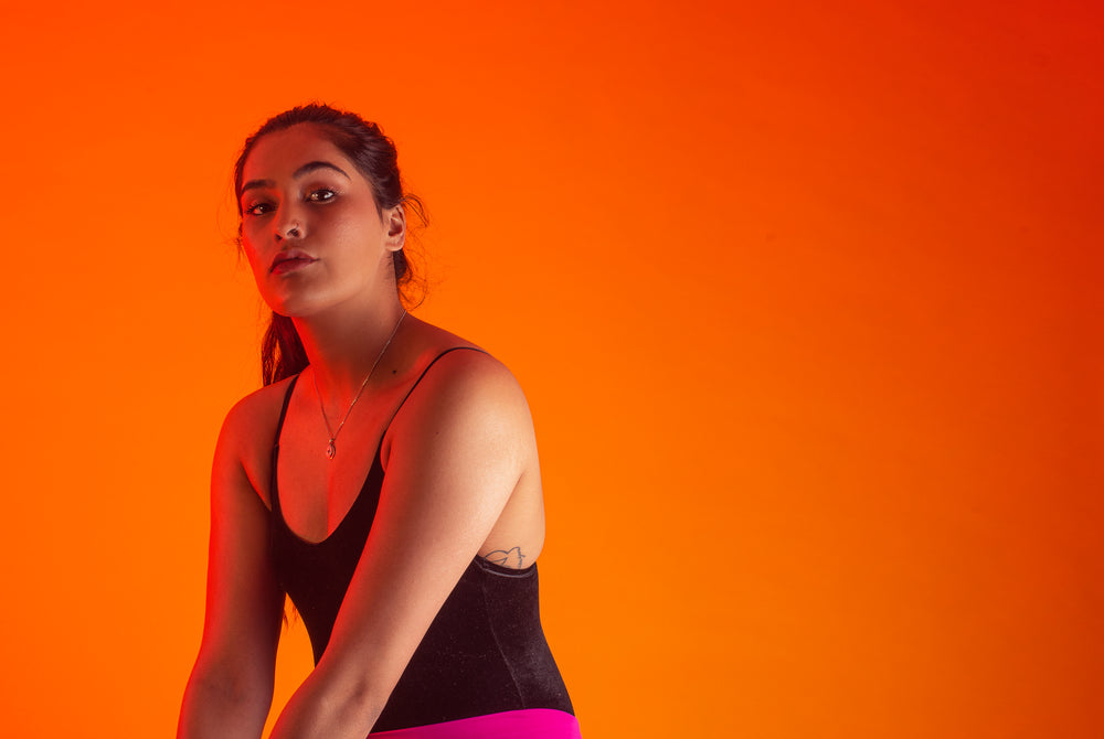 woman wearing black vest poses against orange background