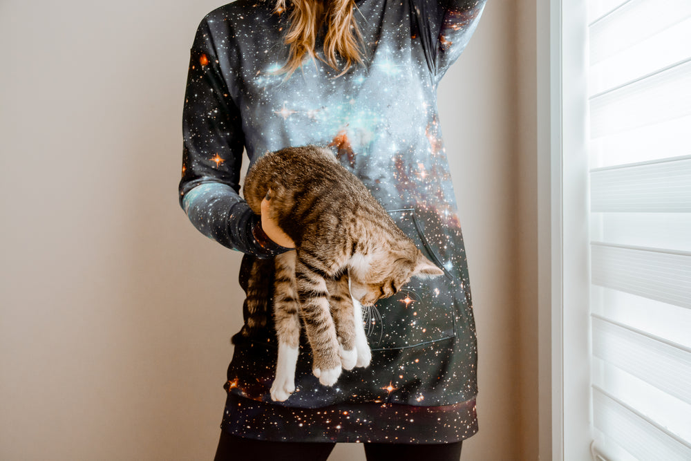 woman wearing hoodie holds cat in one hand