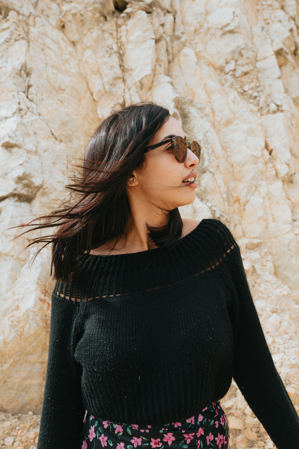 woman wearing sunglasses stands in front of a rocky surface