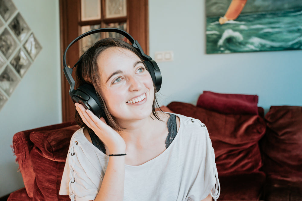 woman wears headphones with one hand up smiling
