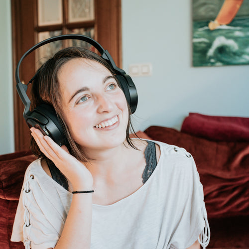 Woman Wears Headphones With One Hand Up Smiling