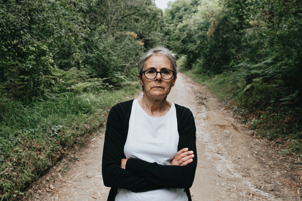 woman with her arms crossed on a tree lined trail