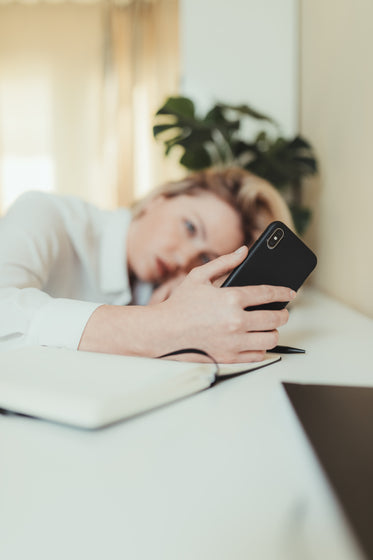 woman with her head down on the table looking at phone