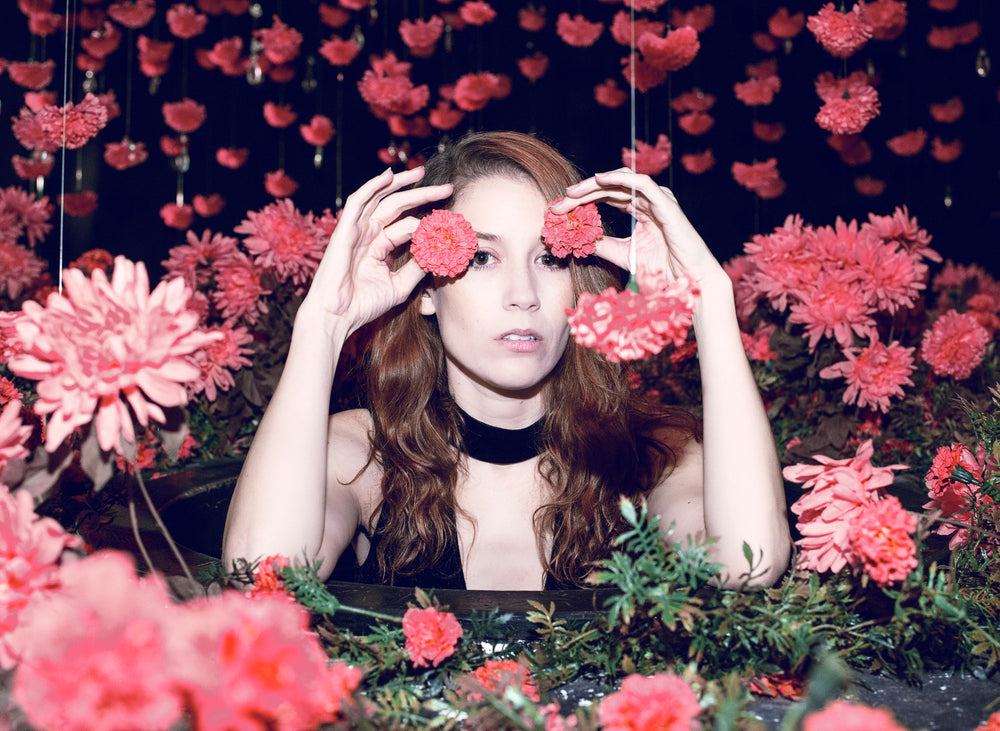 woman with red hair half hides behind red flowers