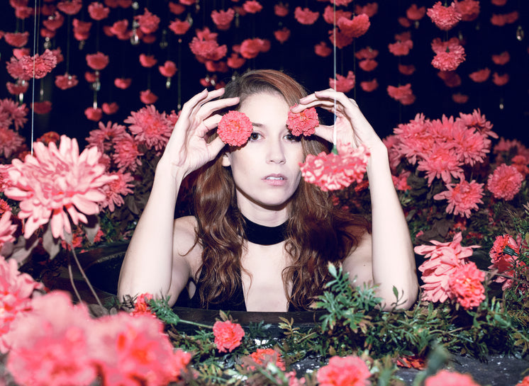 Woman With Red Hair Half Hides Behind Red Flowers