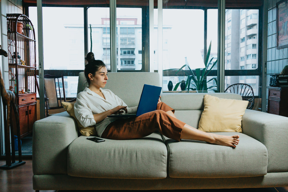 woman works from home on a beige colored couch