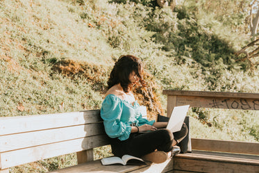 woman works on her laptop on a wooden bench outdoors