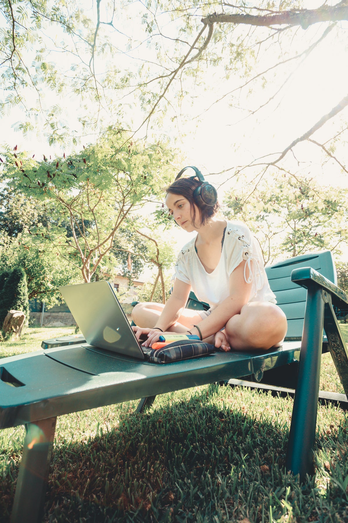 一名妇女坐在户外的绿色躺椅上用笔记本电脑工作