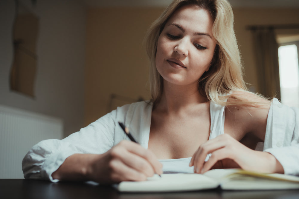 woman writes in a notebook at home on yellow background