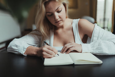 woman writes in her notebook sitting back at a table