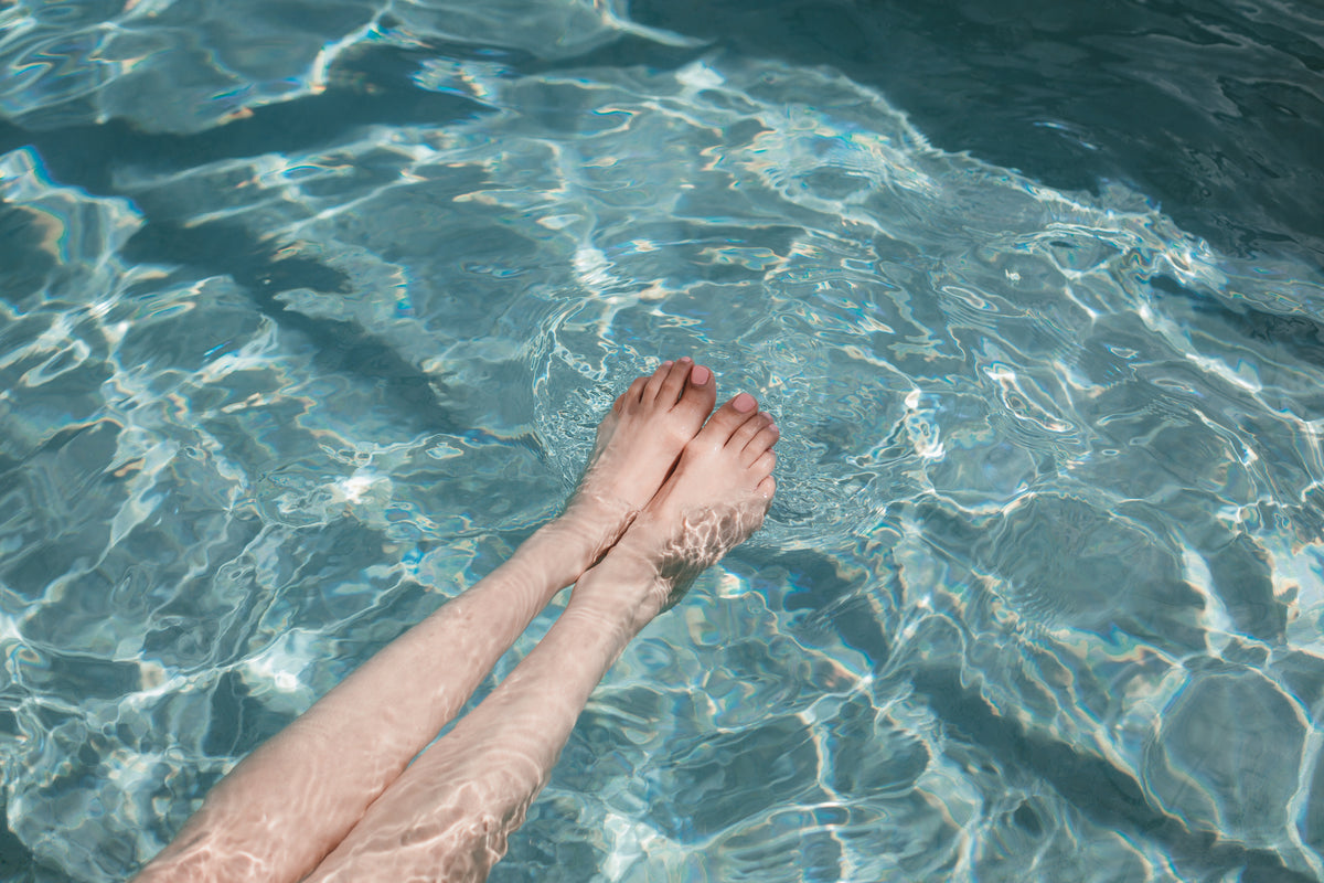 女人的腿伸入泳池，脚趾甲呈粉红色