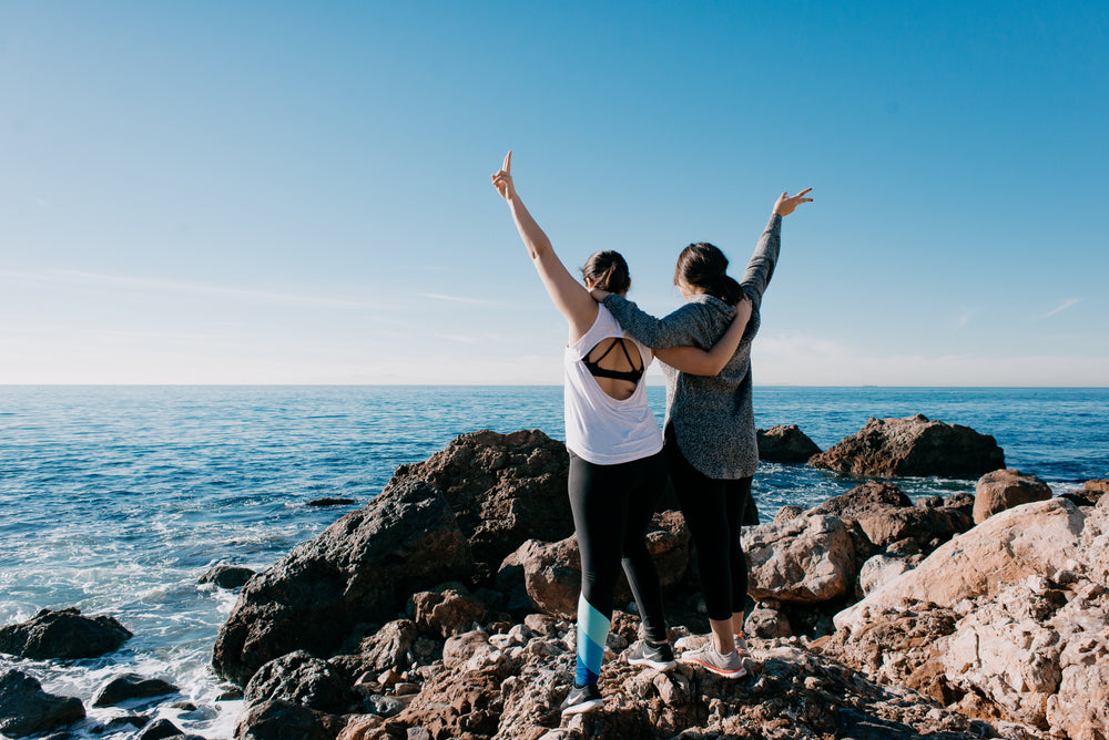 women arm in arm raise their hands in peace sign on beach