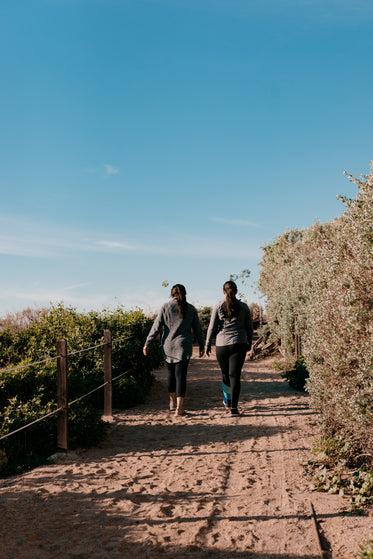 women hike up sandy path surrounded by lush greenery