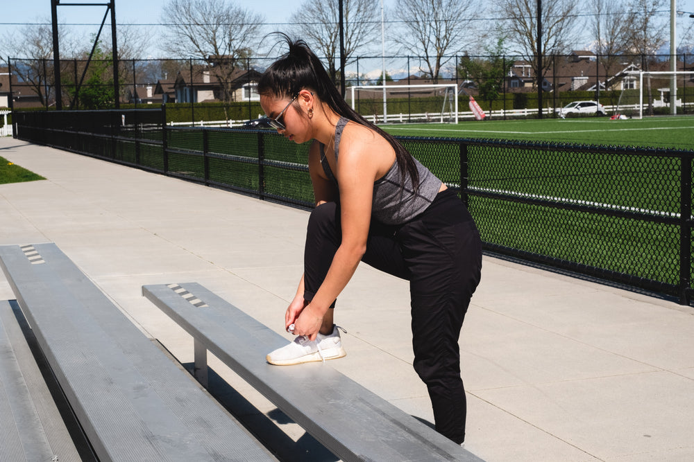 women leans over to tie she shoe on a bench