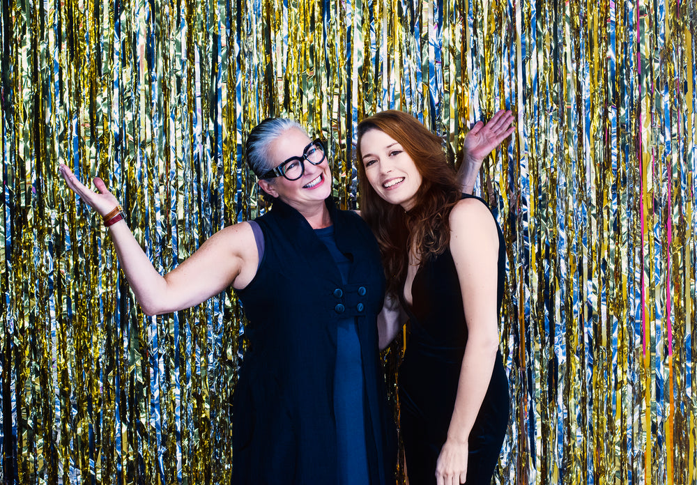 women pose in front of silver and gold metallic streamers