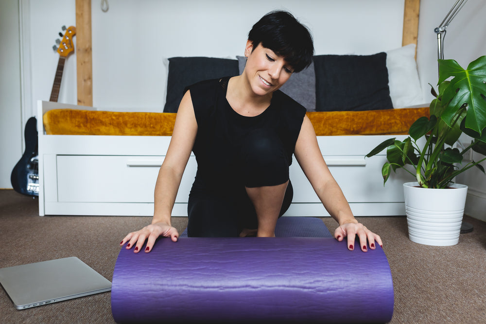 women rolls out a purple yoga mat in her living room