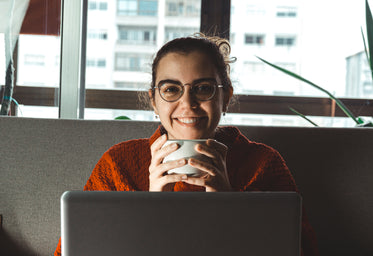 women smiles holding mug sitting behind a laptop