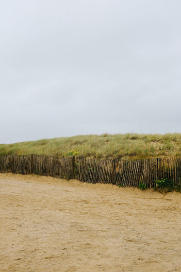 wooden fence lines a sandy beach and grassy hill