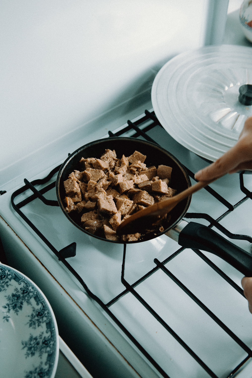 wooden spoon mixes meat in a black frying pan