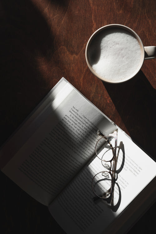 wooden table with latte and open book with glasses