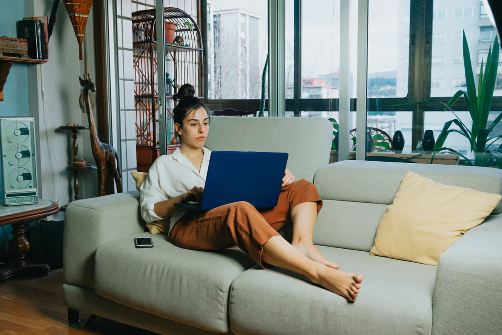 working from a beige couch with a laptop on lap