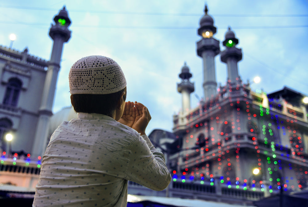 young boy holds hands up outside mosque