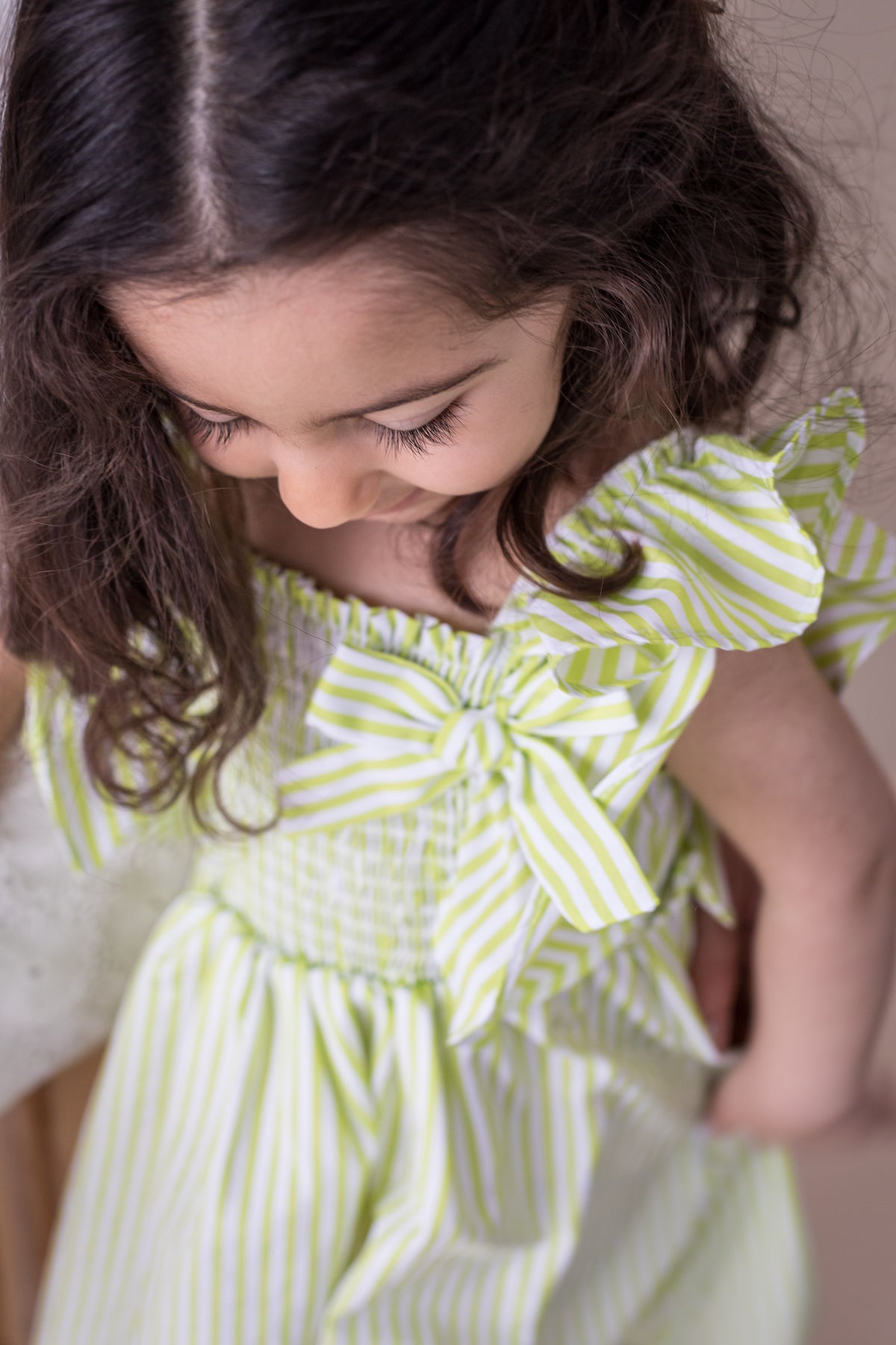 young child in a green and white dress looks down