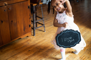 young girl smiles with mom sign