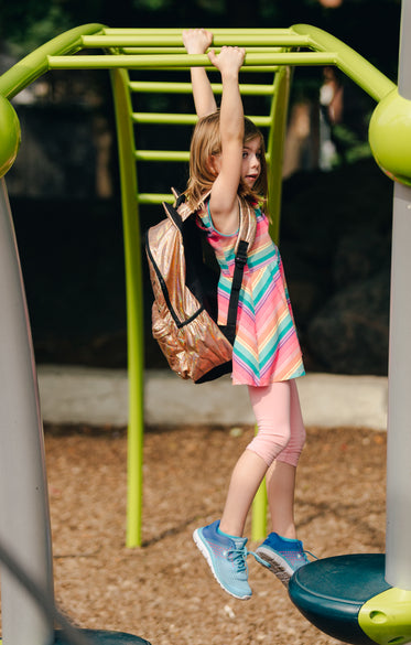 young girl swinging on bars with backpack