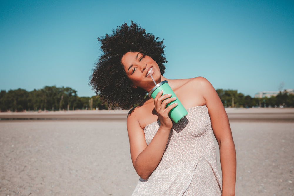 young woman holding drink cup with straw on sandy beach