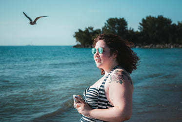 young woman in sunglasses holding camera facing beach