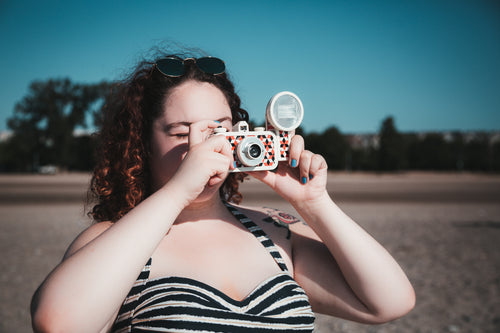 young woman in sunglasses taking photograph on beach