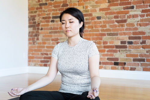 young woman meditating in front of brick wall