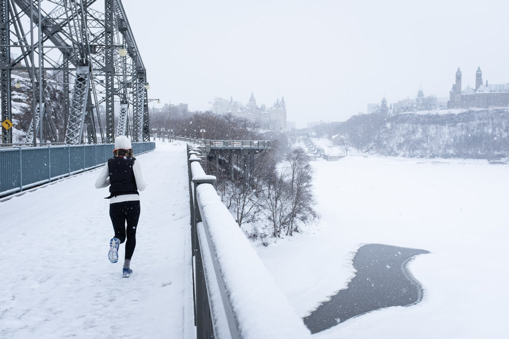 young woman running across a snowy bridge