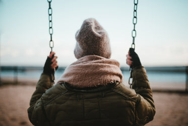 young woman sat on swing in front of beach