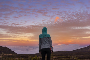 young woman standing on a mountain looking over the clouds