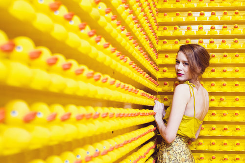 young woman stands by a wall of rubber ducks