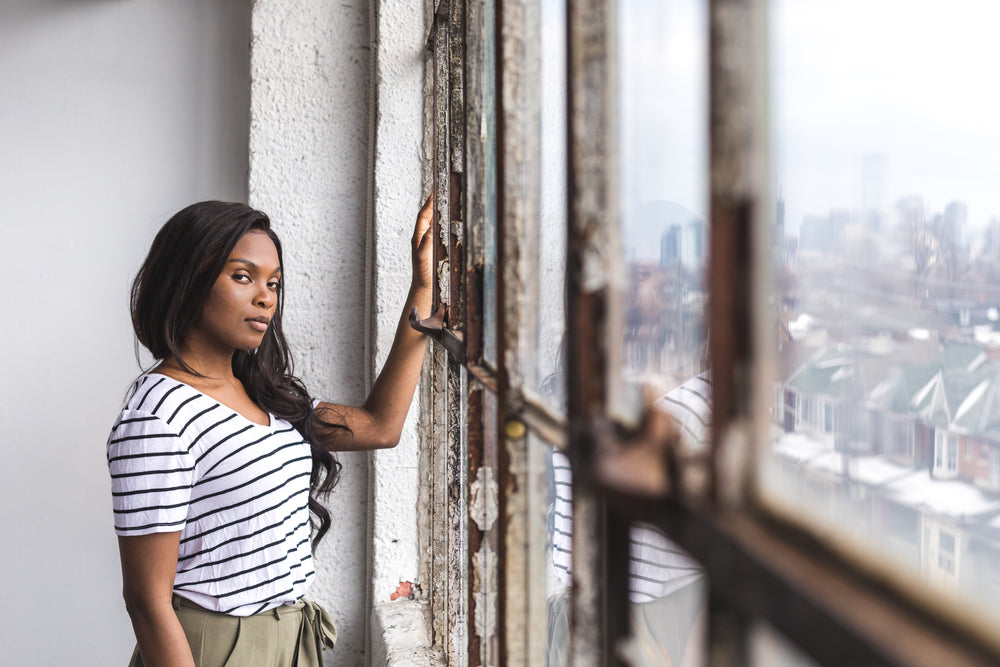 young woman stands in front of an industrial window