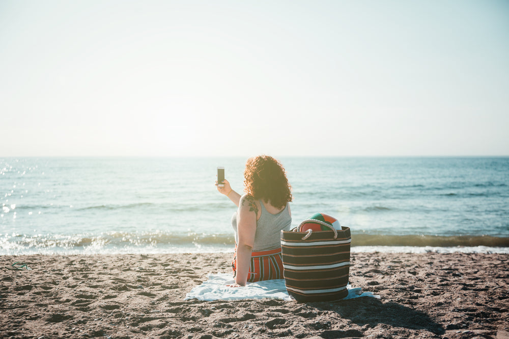 young woman takes selfie while sitting on sunny beach